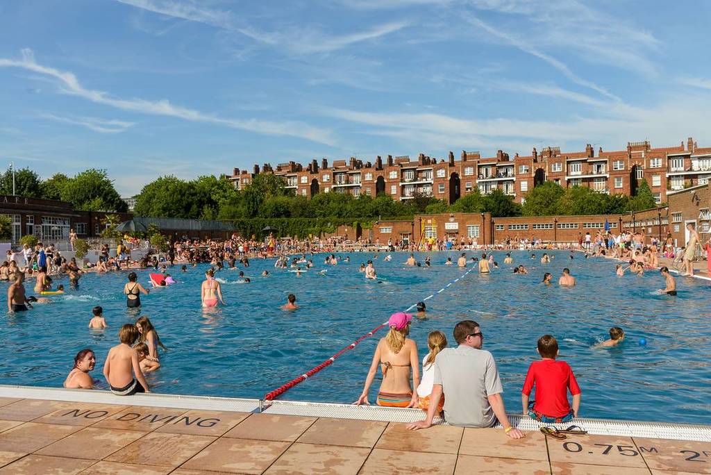 Menschen schwammen hinein und saßen am Rande eines Strandbads in London unter einem strahlend blauen Himmel