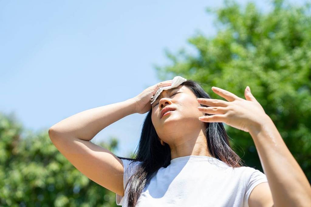 Eine Frau fächert ihr Gesicht mit der Hand auf und wischt sich mit einem Taschentuch über die Stirn, während sie in die Sonne starrt
