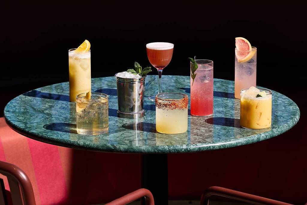 Vari cocktail messicani colorati disposti su un tavolo di marmo turchese scuro tra sedie rosse