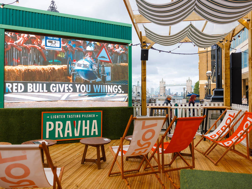 uma área de exibição num bar pop-up com espreguiçadeiras, um ecrã gigante e vista para a Tower Bridge