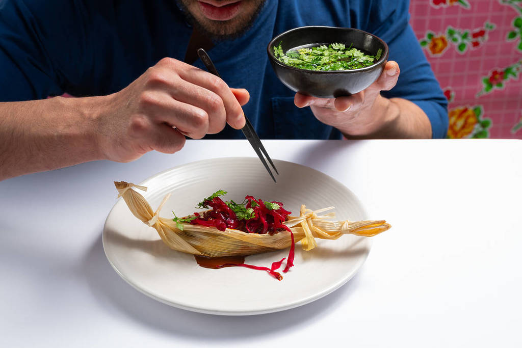 um chef a colocar guarnições verdes num prato de comida artisticamente decorado