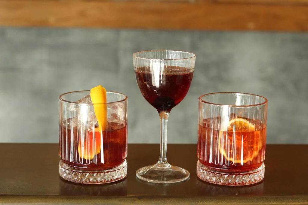 um trio de cocktails envelhecidos em barril, um num copo coupe e os outros em copos de whisky