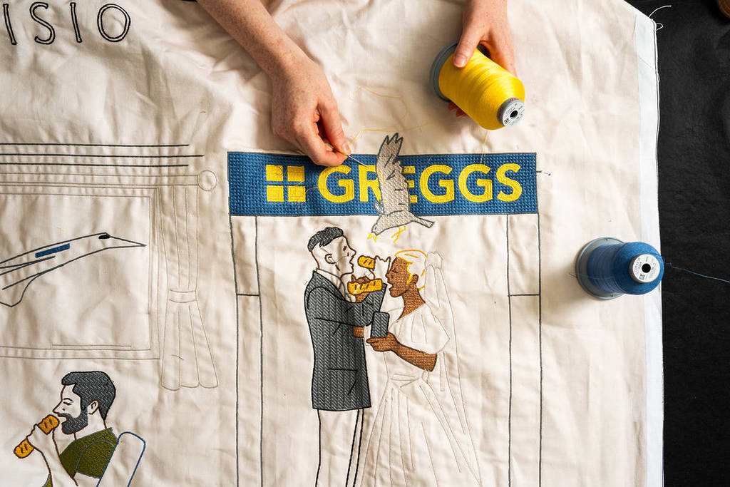 Jemand näht einen Teil eines riesigen Wandteppichs mit Bildern von Menschen, die Greggs-Wurstbrötchen essen