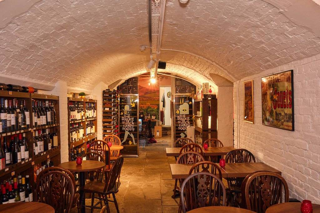 An elegant rustic wine cellar interior with a vaulted ceiling, vintage-style tables and chairs, and wine shelves along the walls