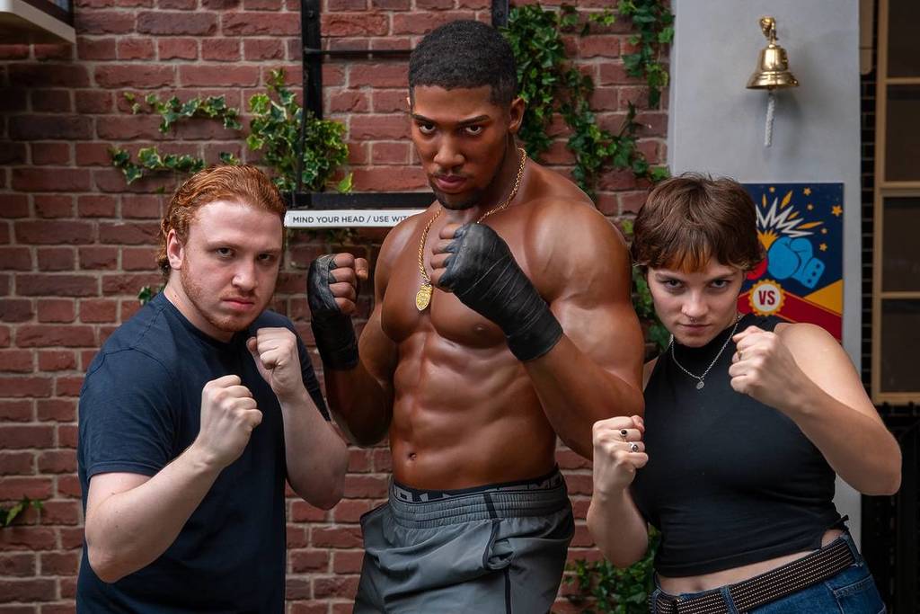 een man en een vrouw poseren met het wassen beeld van Anthony Joshua, beiden met hun vuisten omhoog alsof ze op het punt staan te vechten