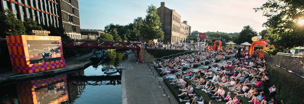 Des gens assis sur les marches au bord du canal à Kings Cross, en train de regarder un film sur un écran géant de l’autre côté du canal