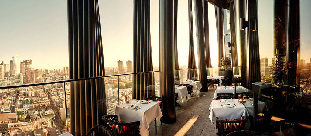 una terrazza sul tetto con tanti tavoli e sedie che si affaccia sullo skyline di Londra