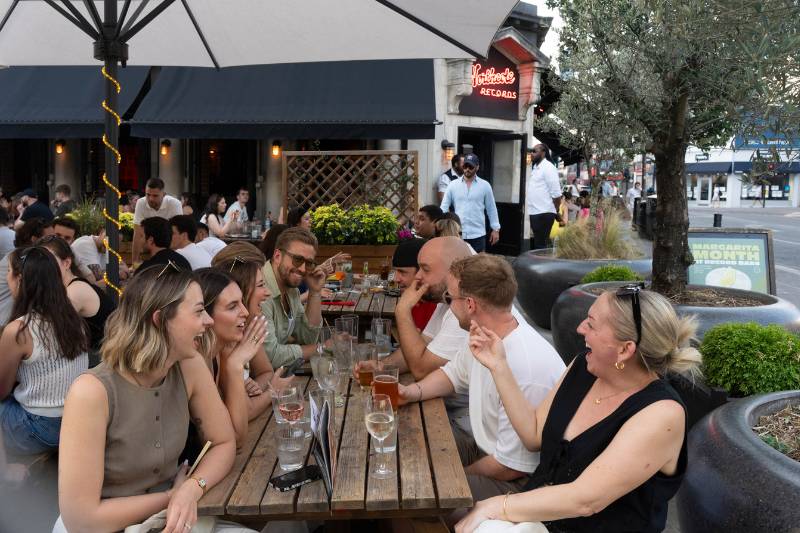 des gens assis sur un banc devant un bar de Northcote Road