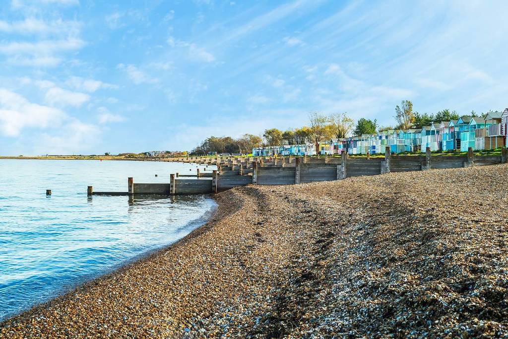 Ein Kiesstrand mit bunten Strandhütten entlang
