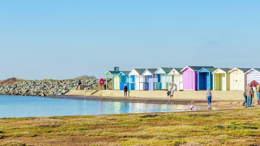 Die Blaue Flagge wurde dem Strand von Brightlingsea verliehen. 2. MÄRZ 2025, Essex, Großbritannien, Strandhütten am sauberen Sandstrand, Leuchtturm, Platz für Text, neue Unterkünfte, spielende Kinder am Strand