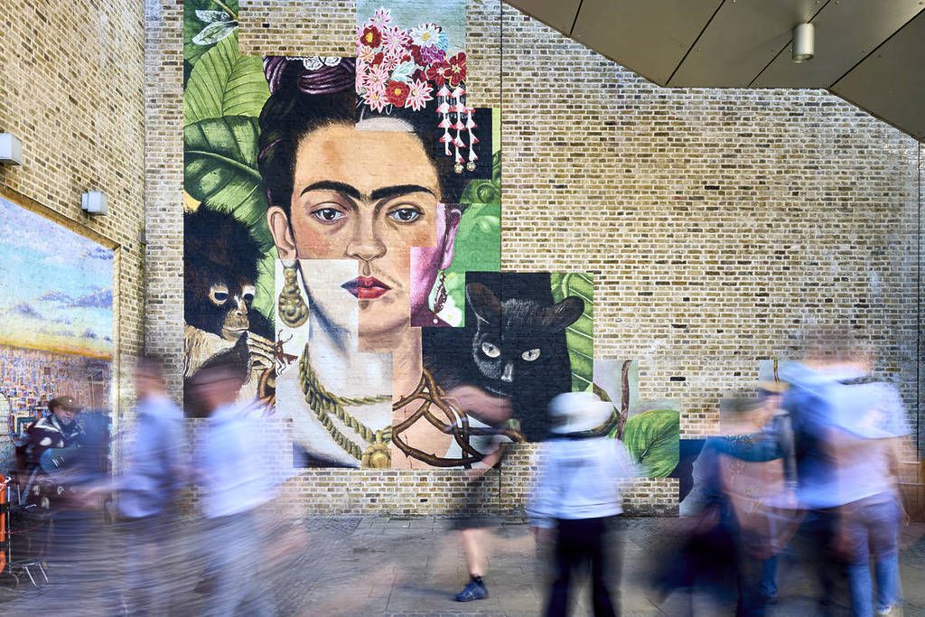 Menschen, die an einem Wandgemälde von Frida Kahlo an einer Wand in London vorbeigehen