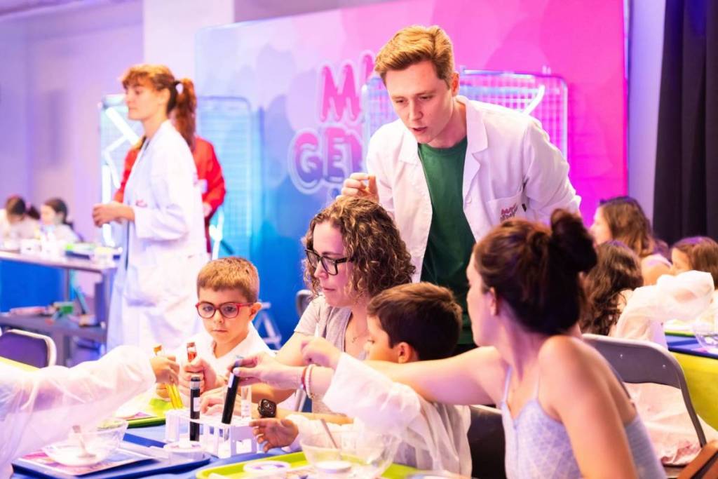 Leute in Laborkitteln zeigen Kindern und Eltern Experimente