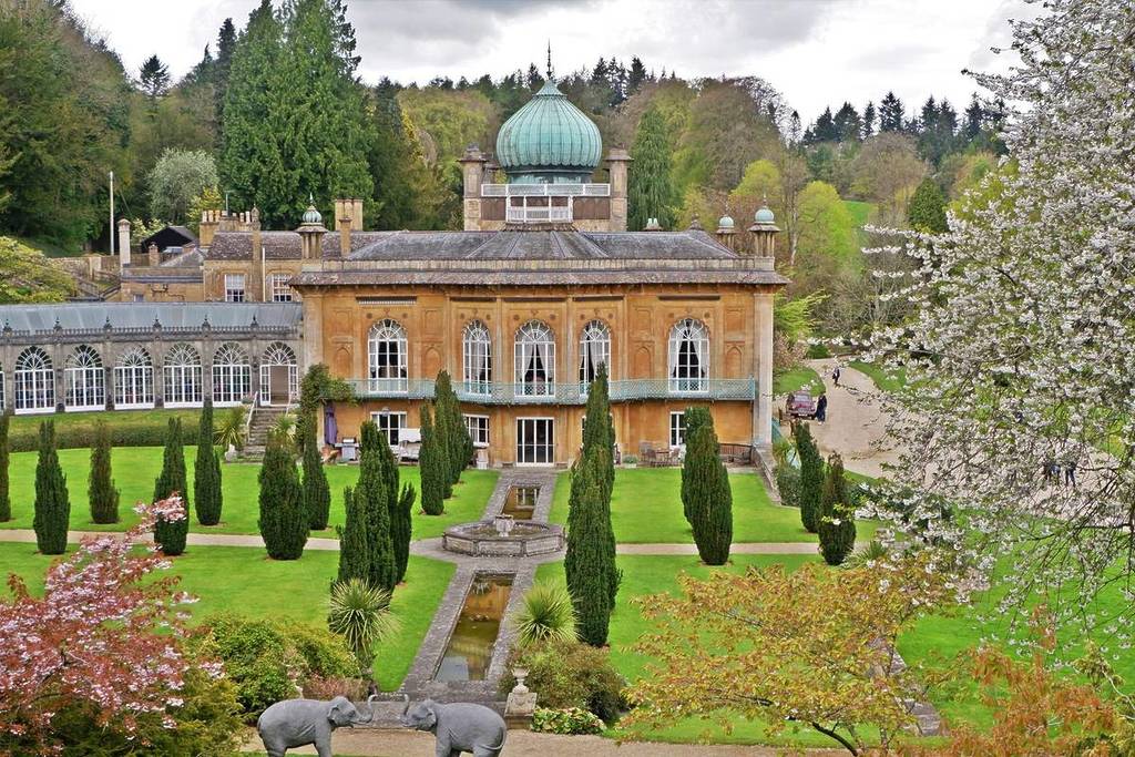 Sezincote-Haus mit seinem blauen Kuppeldach, üppigen grünen Gärten und zwei Elefantenstatuen im Vordergrund.