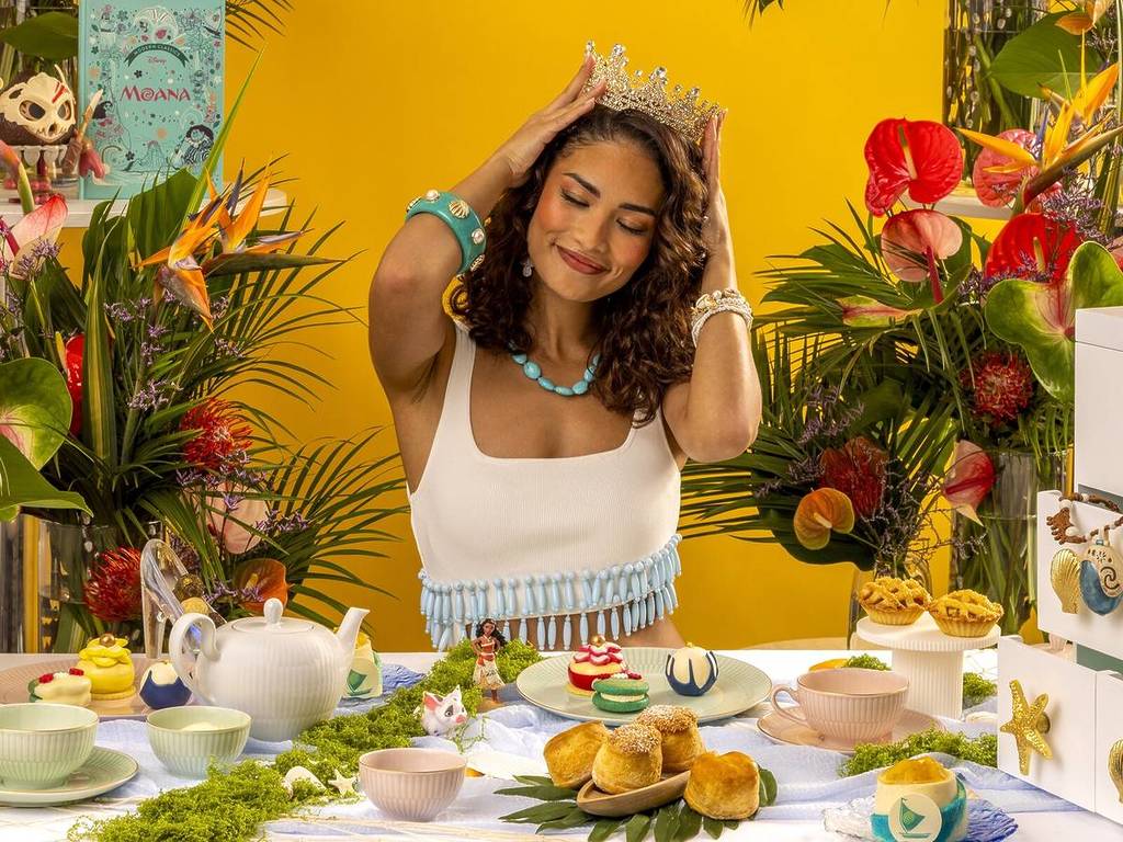 Jemand saß da ​​und hielt eine Krone an den Kopf, hinter einer Reihe von Nachmittagstee-Leckereien im Moana-Stil