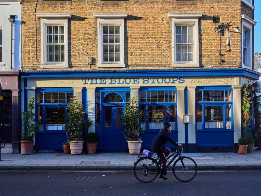 Jemand fährt mit dem Fahrrad an einem Pub mit blauer Fassade vorbei