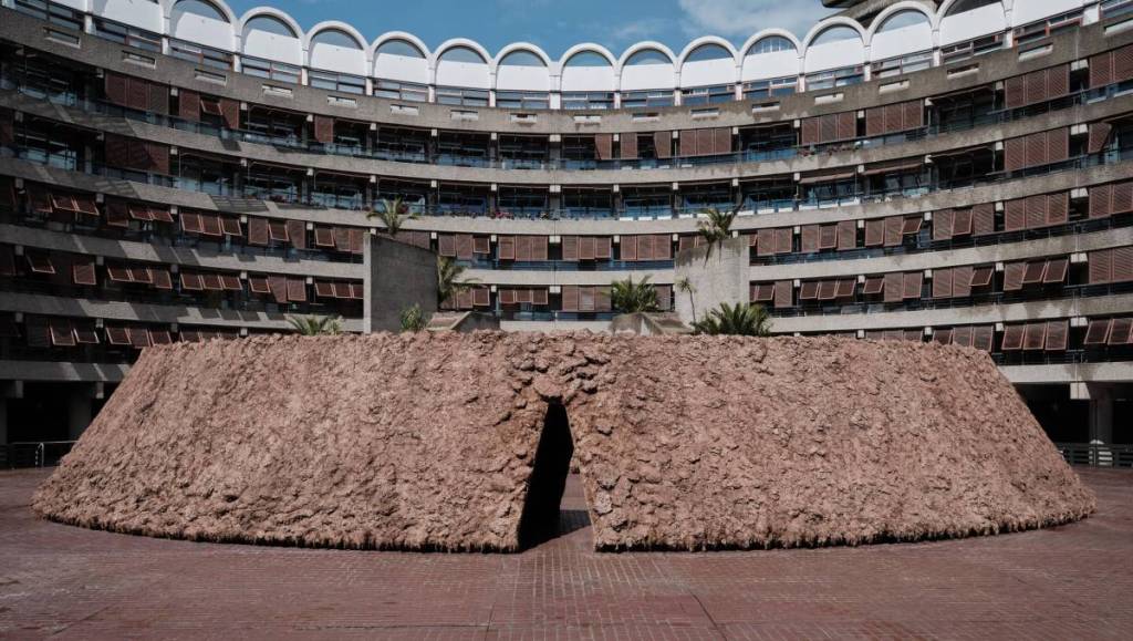 Une installation artistique dans la cour du Barbican, composée d’un grand monticule d’argile et de terre, avec une entrée vers l’intérieur