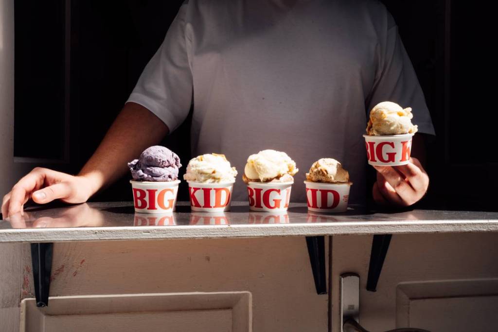 une rangée de coupes de glaces de différentes saveurs sur un comptoir, avec quelqu'un debout derrière, tenant une des coupes