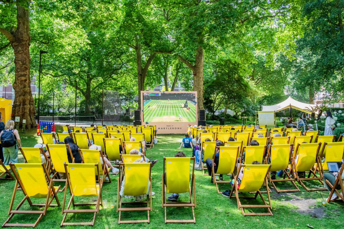 une projection en plein air de Wimbledon dans un parc, avec un grand écran et plein de transats jaunes