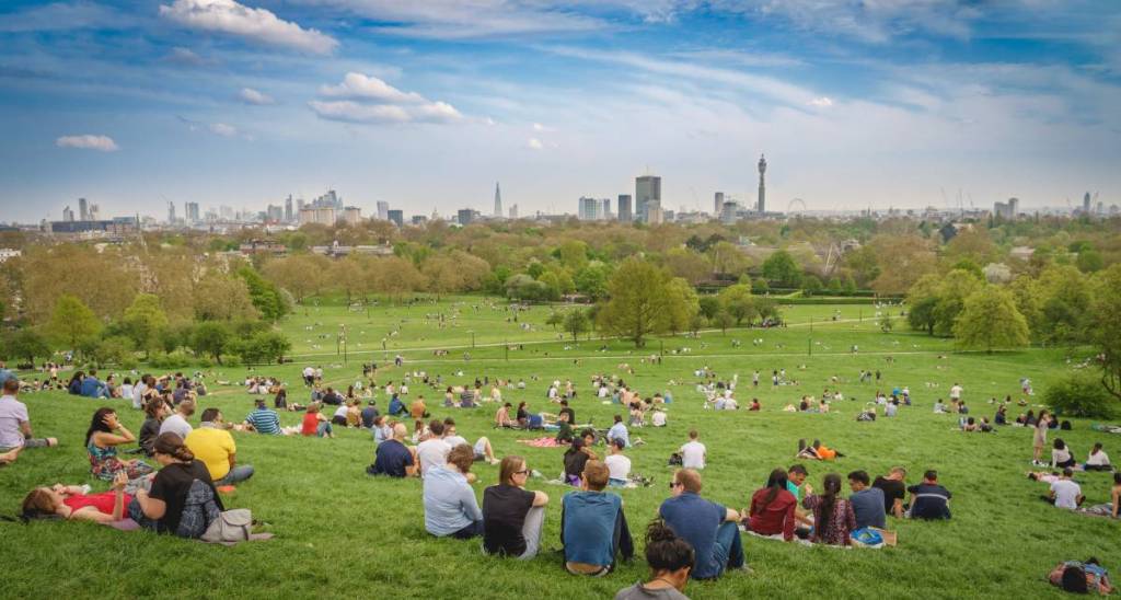 Menschen saßen in Gruppen auf dem Primrose Hill und blickten auf die Skyline in der Ferne