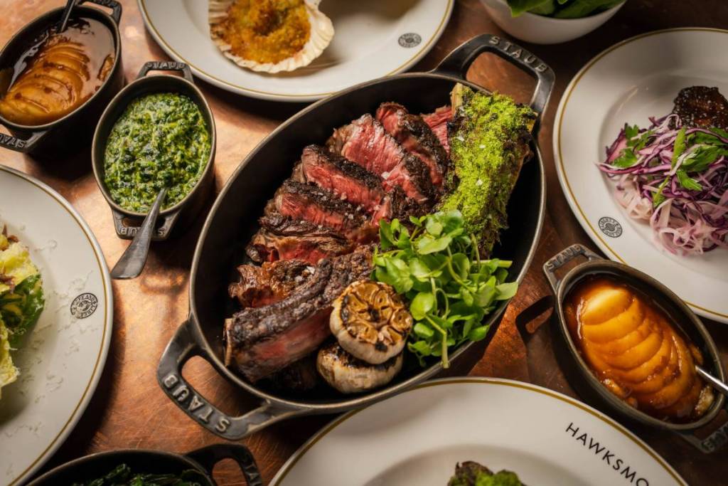 un impressionnant steak cuit à la poêle au milieu d’une table bondée de plats