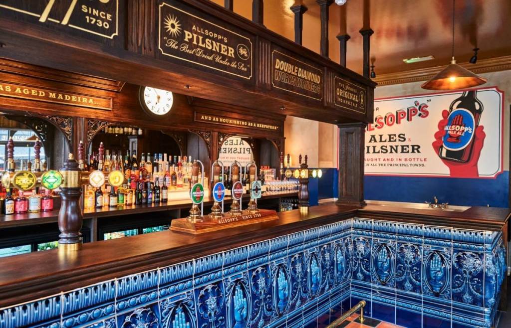 Die Blue Stoops Bar mit dunklem Holz, blauen Zierfliesen, Handpumpen und Vintage-Werbung von Allsopp's.