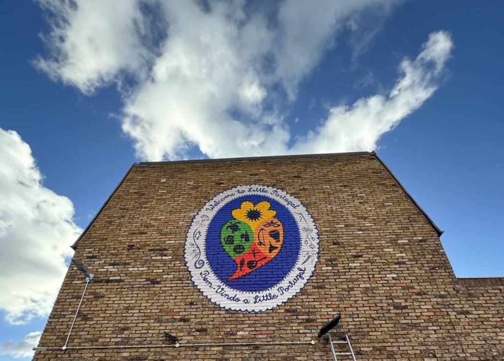 Un murale con la scritta “benvenuti a Little Portugal” sulla facciata di un edificio sotto un cielo azzurro