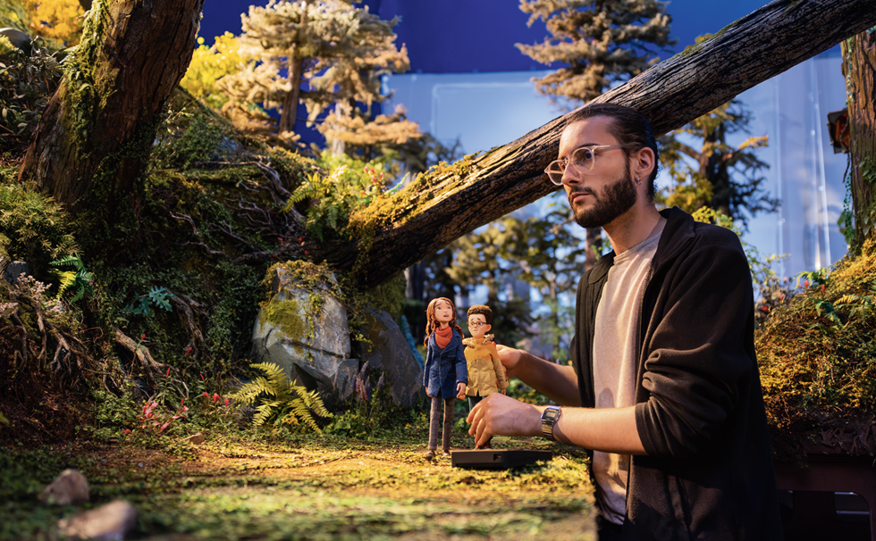 a behind the scenes shot of someone moving stop-motion figurines in a forest-like setting