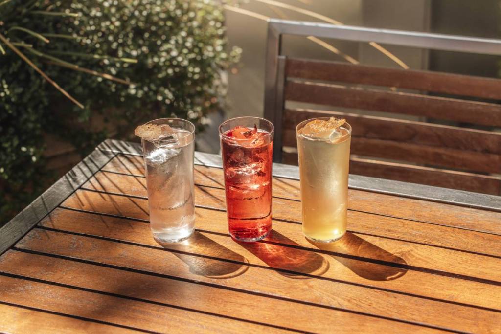 Drei farbenfrohe Cocktails, serviert in der Sonne auf einem Holztisch
