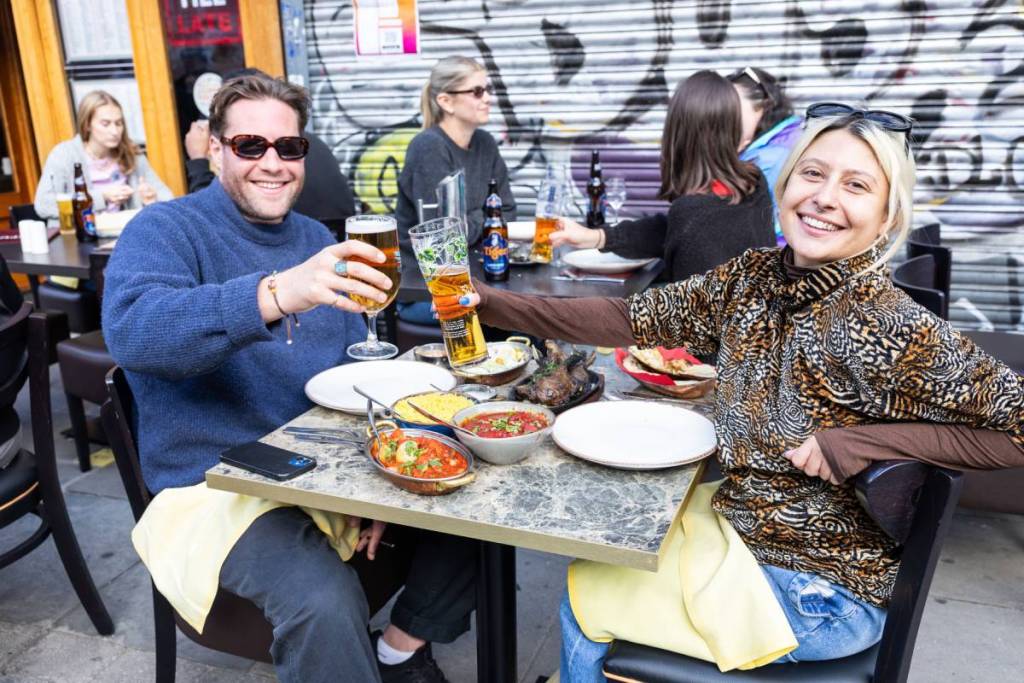 des gens qui trinquent avec leur bière tout en dégustant un curry à une table en terrasse