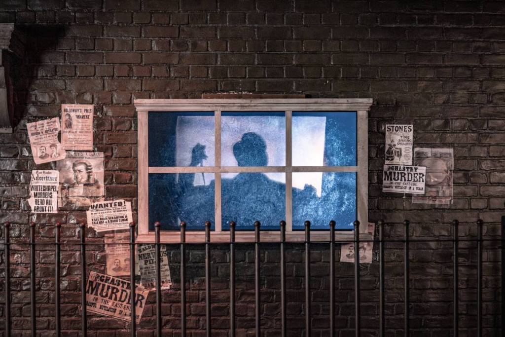 Eine Silhouette von Jack the Ripper reckt ein Messer in einem Fenster empor, umgeben von Steckbriefen und Zeitungsausschnitten