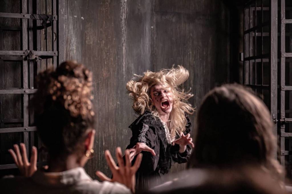 Eine als „Hexe“ verkleidete Darstellerin, Elizabeth Sawyer, schreit und stürzt sich auf zwei Frauen, die die London Dungeons besuchen