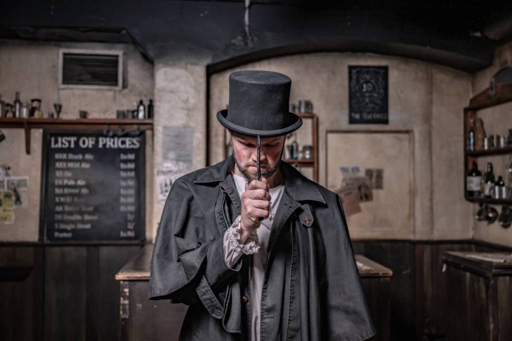 ein als Jack the Ripper verkleideter Schauspieler, mit Staubmantel und Zylinder, hält ein Rasiermesser vor sein Gesicht