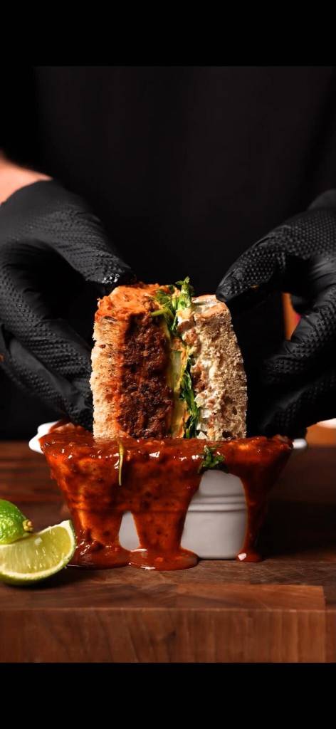 um sanduíche de carne birria a ser mergulhado numa panela de consomê
