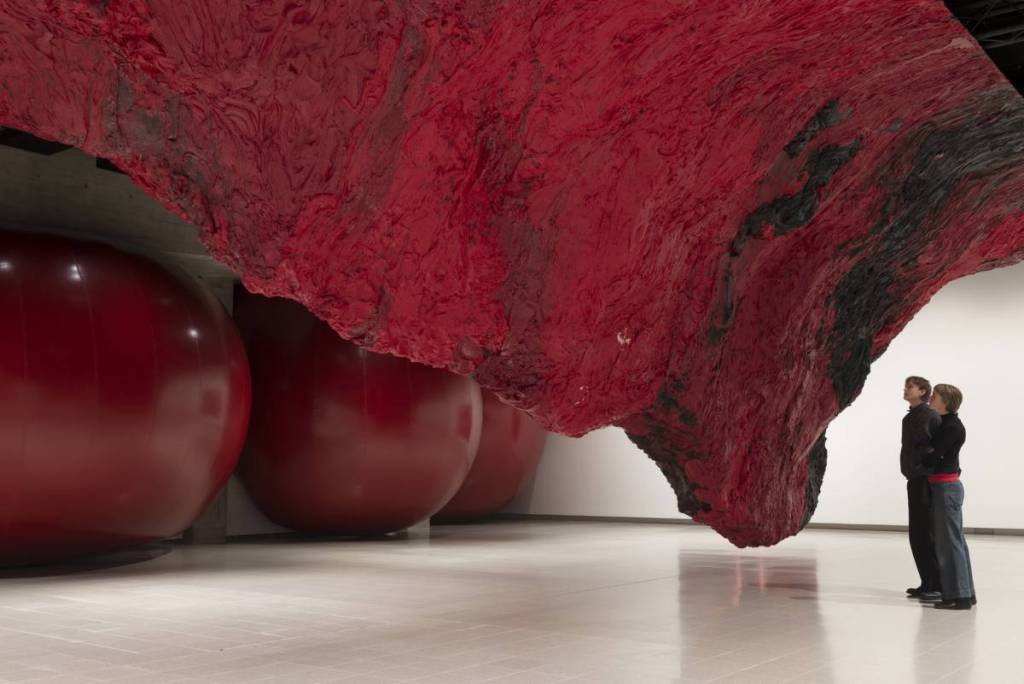 Twee mensen stonden onder een indrukwekkend groot rood-zwart beeld dat vanaf het plafond naar beneden torent als een omgekeerde berg of een vreemde organische levensvorm