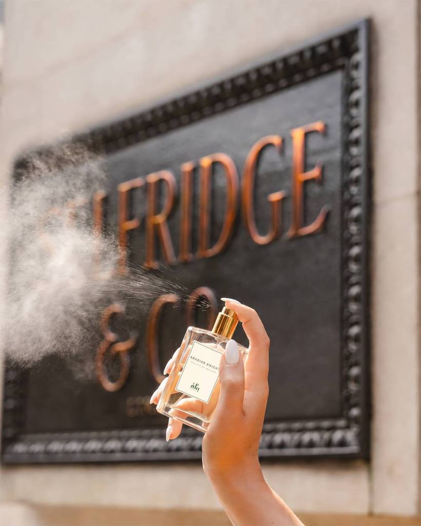 hand spraying batlah perfume into the air in front of the selfridges plaque
