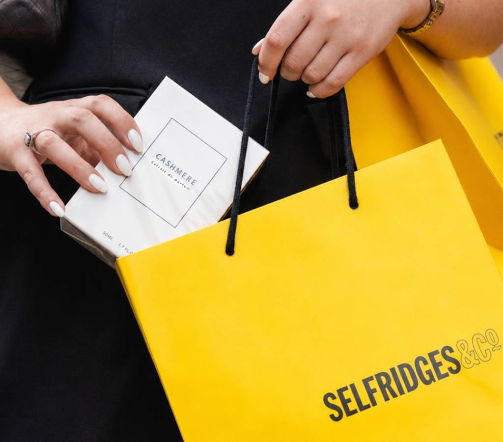 woman places a batlah perfume into a yellow selfridges bag