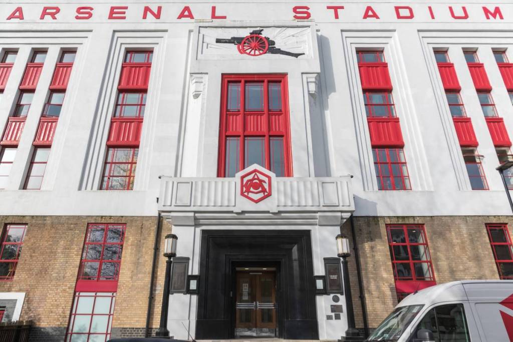 La fachada de un edificio, pintada de rojo y blanco con el escudo de los Gunners y la inscripción «Arsenal Stadium»