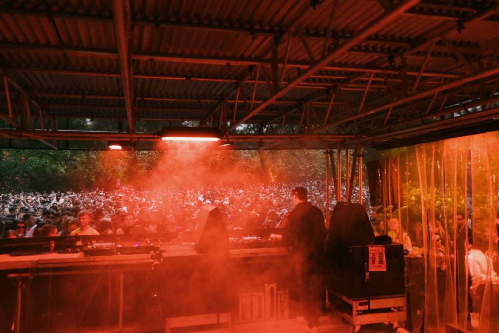 A DJ in a booth with red lighting and smoke machine plays to a crowd at RALLY Festival