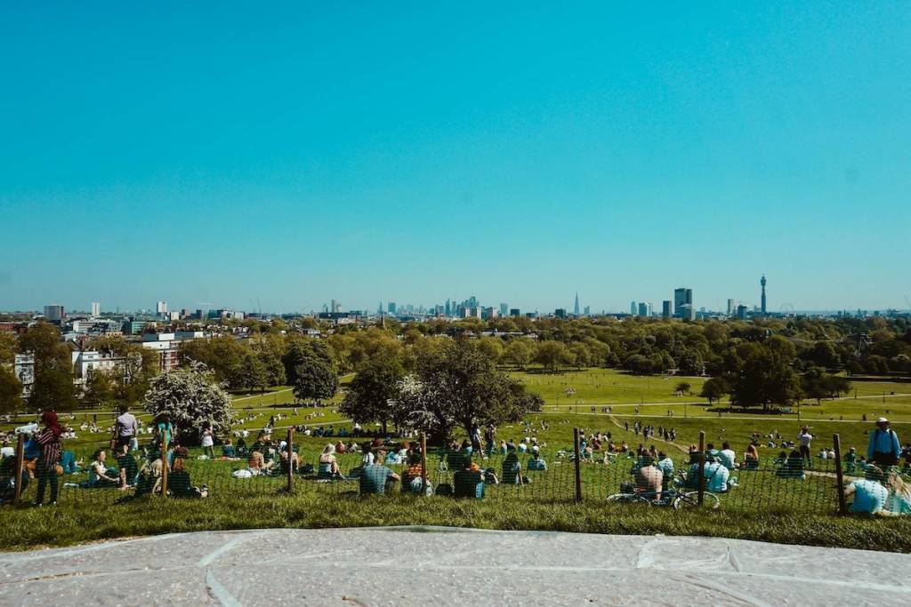 a view of london skyline from primrose hill, with blue skies and people sitting on the grass