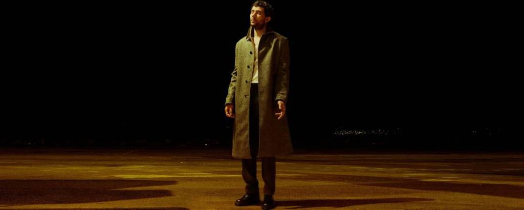 l’attore Josh O’Connor in piedi sull’asfalto in una scena buia e vuota, immerso in una luce dorata con gli occhi chiusi
