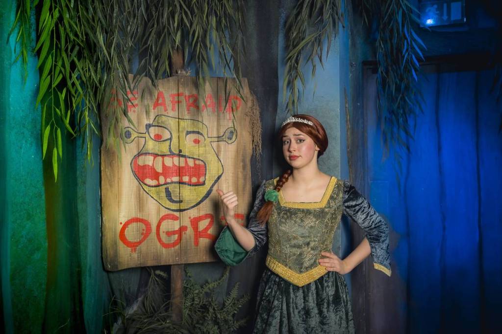 Een vrouw verkleed als Fiona uit Shrek staat naast een bordje met ‘bang ogre’ bij Shrek’s Adventure London