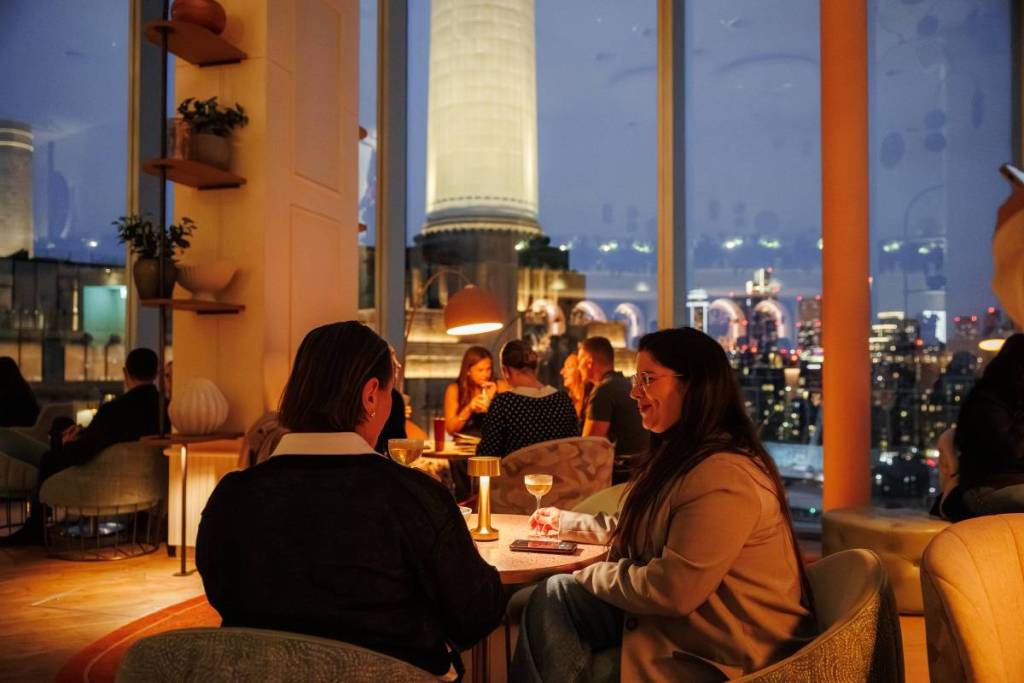persone che si godono i cocktail in un bar dalla luce soffusa con grandi finestre che si affacciano su una delle ciminiere di Battersea e su Londra