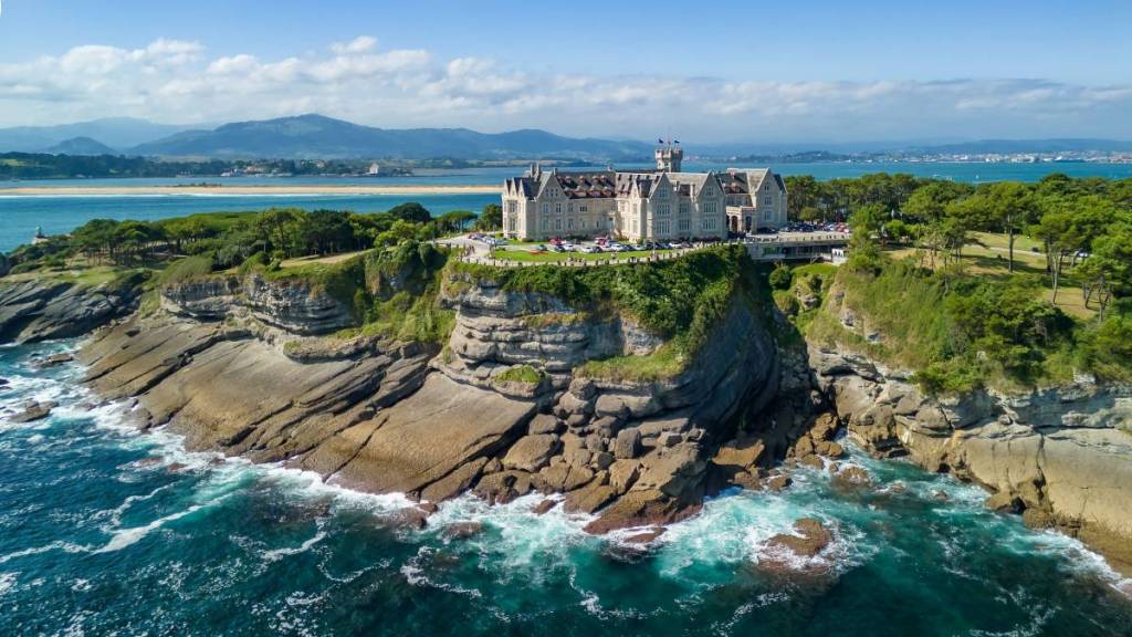 Une vue aérienne du palais de Magdalena : un bâtiment à l’allure majestueuse perché au sommet d’une falaise, entouré par la mer