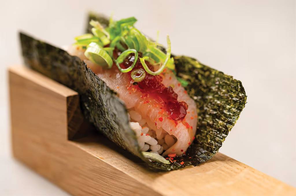 una delicada porción de pescado coronada con cebolleta finamente cortada en un temaki, un rollito de sushi hecho a mano