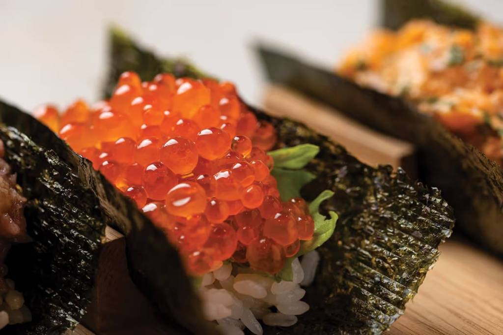 un primer plano de las huevas de pescado sobre un temaki, un rollito de sushi hecho a mano