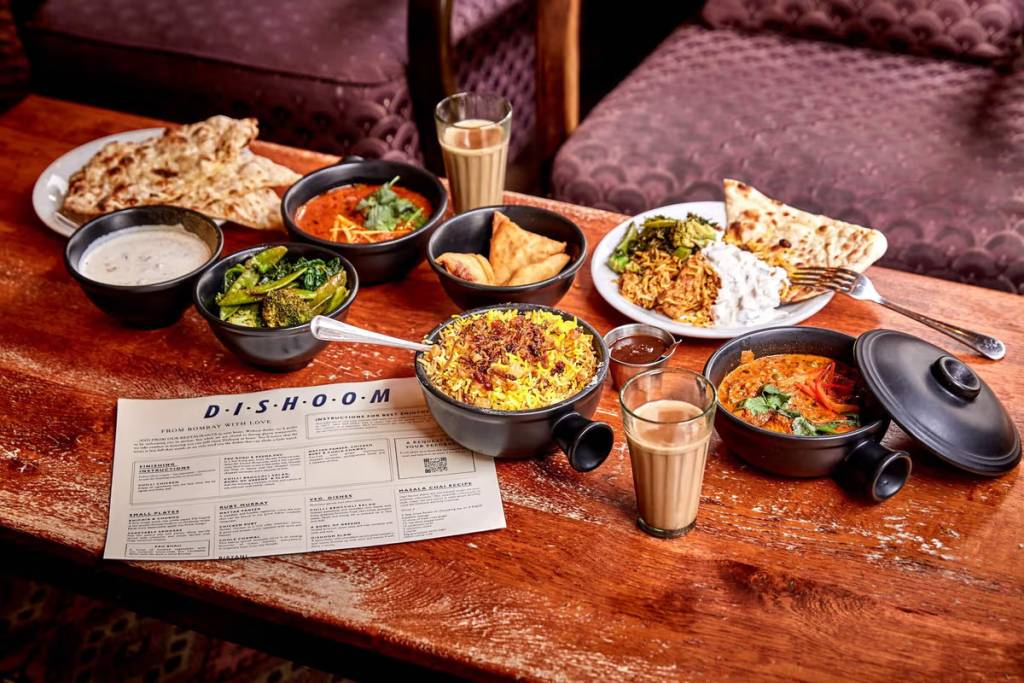 een salontafel vol met eten, zoals rijst, curry’s, naan en chai.