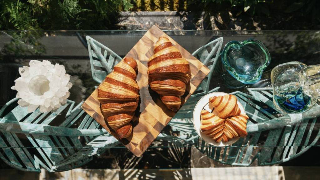 una vista dall’alto di bellissimi croissant disposti su un tagliere appoggiato a un bancone di marmo, accanto a un piattino con dei mini croissant