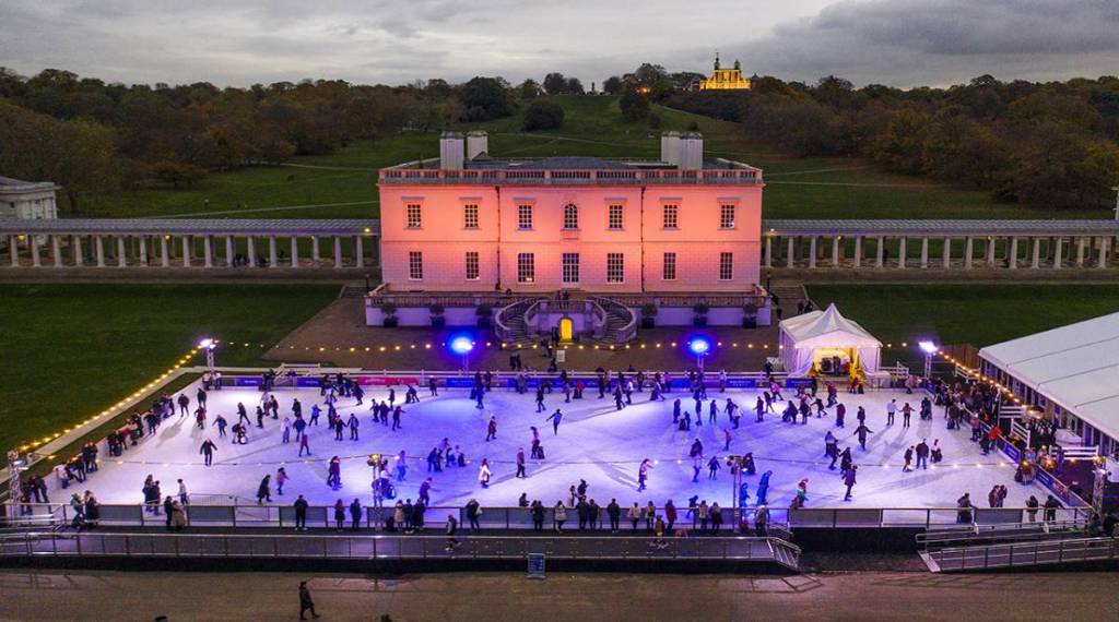 la splendida pista di pattinaggio della Queens House a Greenwich, con una grande pista da pattinaggio immersa nella luce viola e la gente che pattina, davanti alla maestosa Queens House