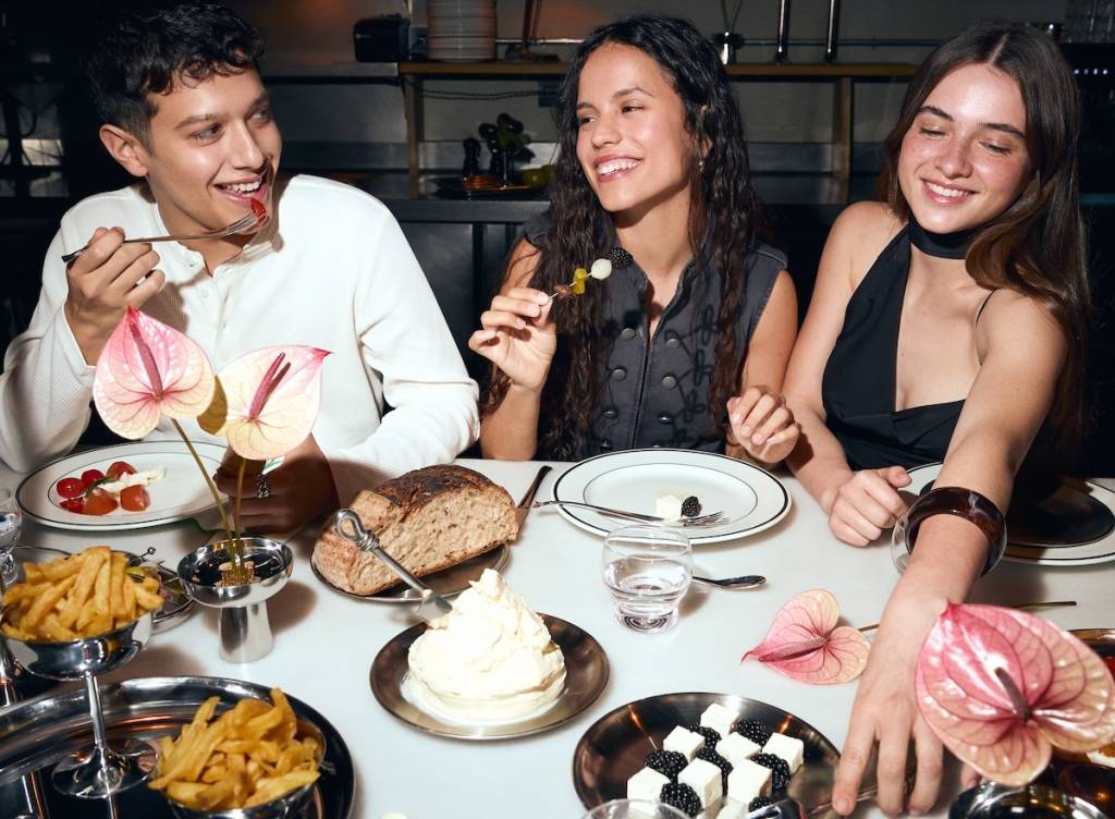 a group of friends, a man and two women, sit at a dining table and help themselves to dishes