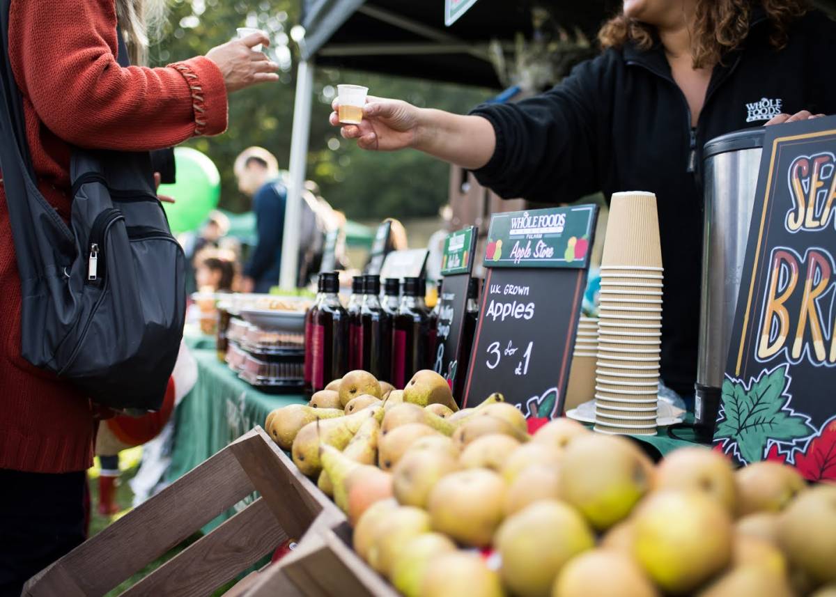 a sample of apple juice being handed to someone over an apple drinks cart at the
